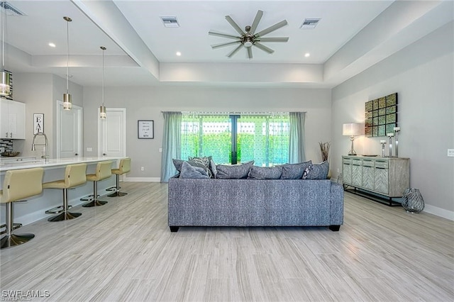 living room with light hardwood / wood-style floors, sink, a raised ceiling, and ceiling fan