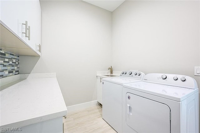 clothes washing area featuring sink, light wood-type flooring, cabinets, and separate washer and dryer