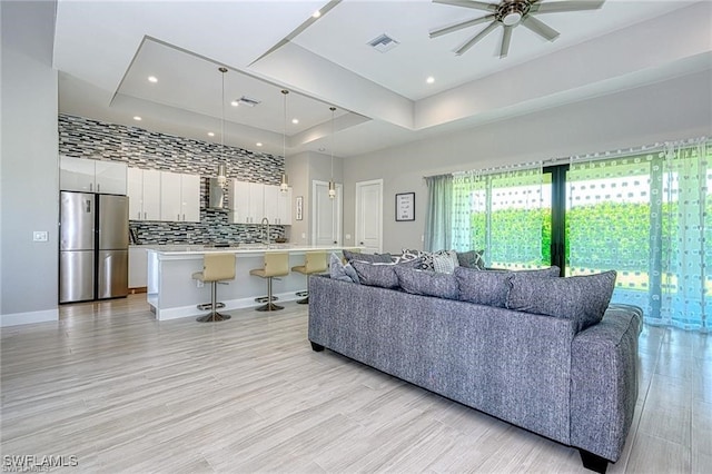 living room with sink, a tray ceiling, light wood-type flooring, and ceiling fan