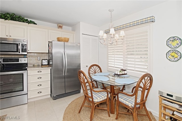 kitchen with light tile patterned flooring, appliances with stainless steel finishes, decorative backsplash, hanging light fixtures, and a notable chandelier