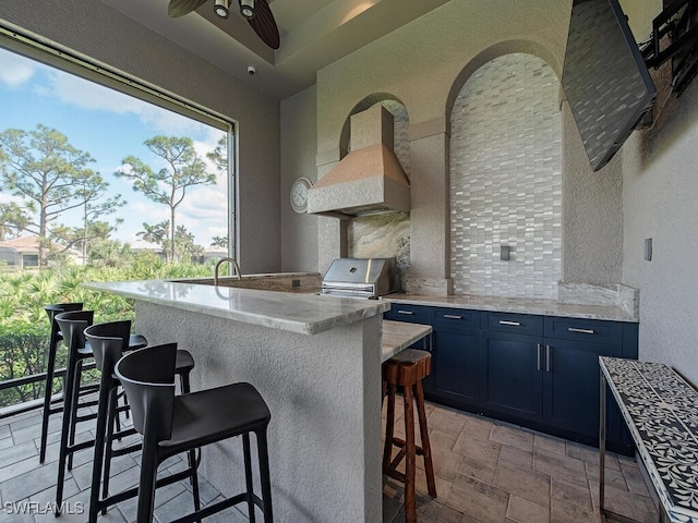 kitchen with sink, a kitchen bar, tasteful backsplash, blue cabinetry, and ceiling fan