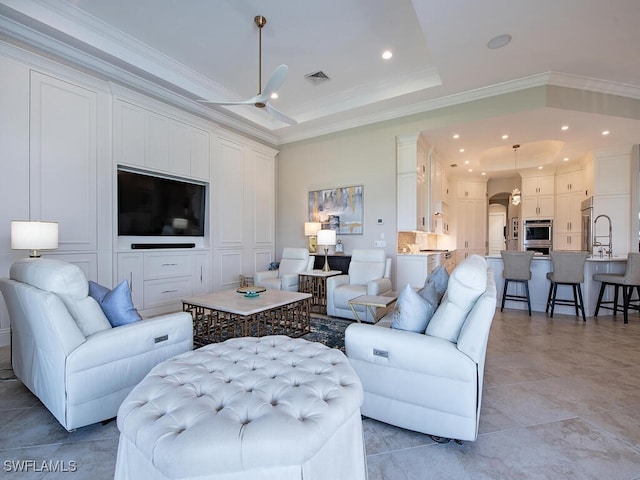 living room with crown molding, light tile patterned flooring, a tray ceiling, and ceiling fan