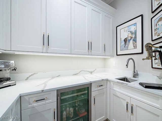 kitchen featuring white cabinetry, wine cooler, light stone countertops, and sink