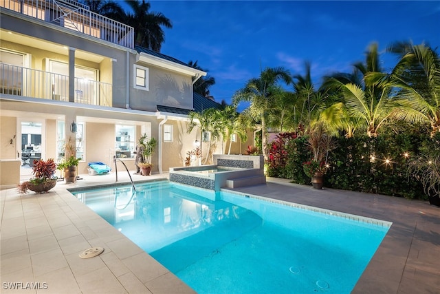 pool at dusk featuring an in ground hot tub and a patio