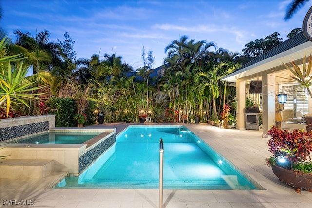 pool at dusk with an in ground hot tub and a patio