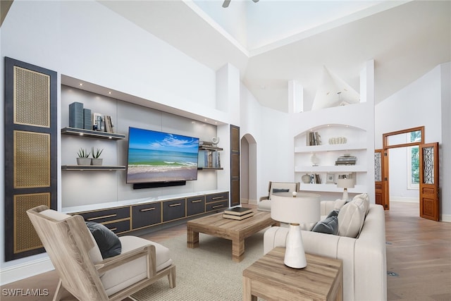 living room with built in shelves, a towering ceiling, and wood-type flooring