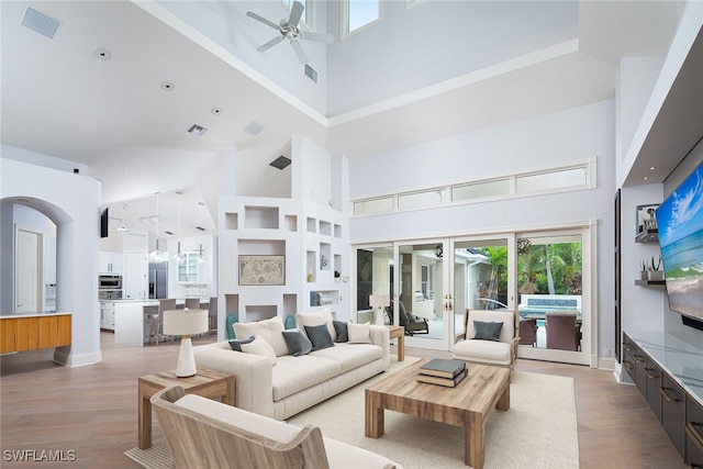 living room featuring ceiling fan, a high ceiling, and light wood-type flooring