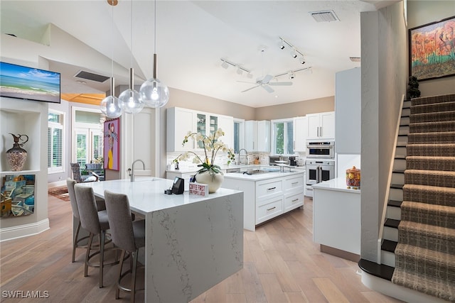 kitchen with hanging light fixtures, double oven, light hardwood / wood-style floors, a kitchen island with sink, and white cabinets