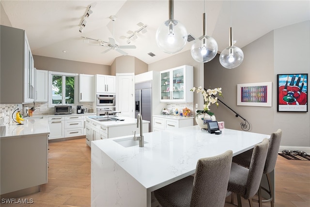 kitchen featuring white cabinetry, hanging light fixtures, tasteful backsplash, a kitchen island with sink, and stainless steel built in fridge