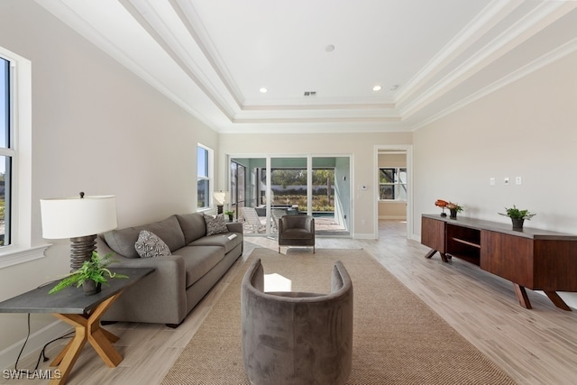 living room with a raised ceiling, ornamental molding, and light wood-type flooring