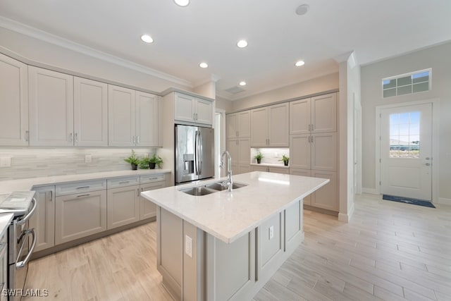 kitchen with backsplash, an island with sink, stainless steel appliances, light hardwood / wood-style floors, and light stone counters