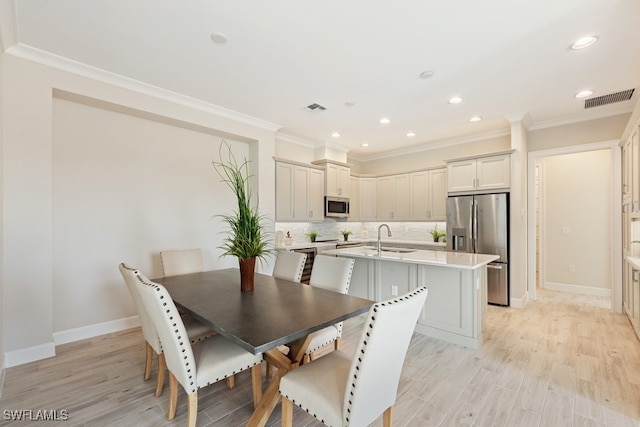 dining room with ornamental molding, sink, and light wood-type flooring