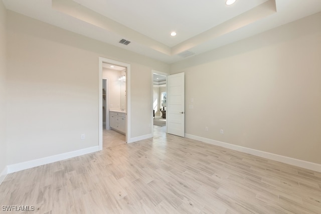 unfurnished bedroom with ensuite bath, a tray ceiling, and light wood-type flooring