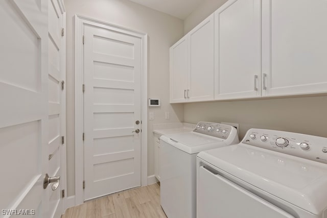 laundry area featuring independent washer and dryer, light wood-type flooring, and cabinets