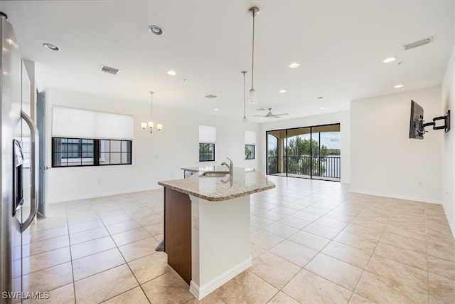 kitchen featuring sink, hanging light fixtures, light stone counters, a kitchen island with sink, and ceiling fan with notable chandelier