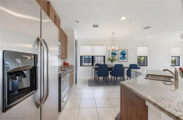 kitchen with pendant lighting, sink, appliances with stainless steel finishes, a notable chandelier, and light stone counters