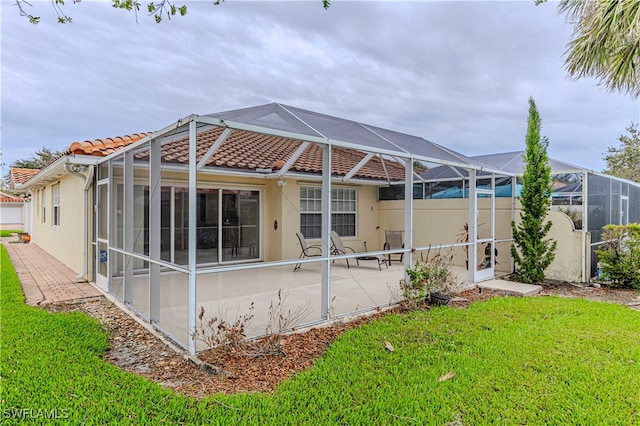 rear view of house featuring a lawn, glass enclosure, and a patio