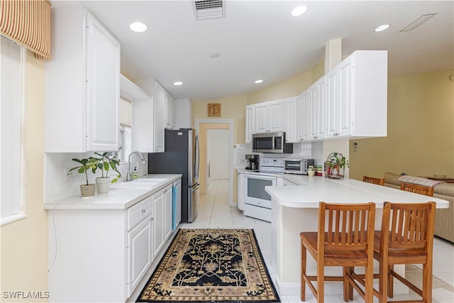 kitchen featuring kitchen peninsula, appliances with stainless steel finishes, a breakfast bar, and white cabinetry