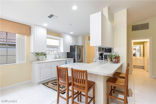 kitchen featuring white cabinetry, sink, kitchen peninsula, stainless steel fridge, and a kitchen bar