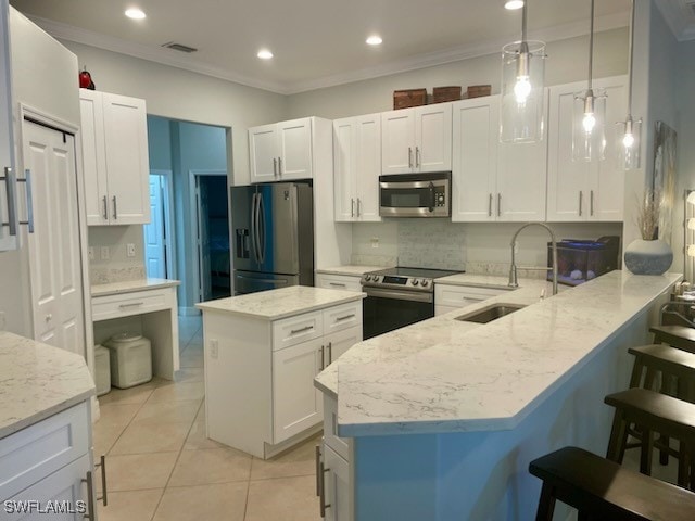 kitchen with appliances with stainless steel finishes, kitchen peninsula, white cabinets, and pendant lighting