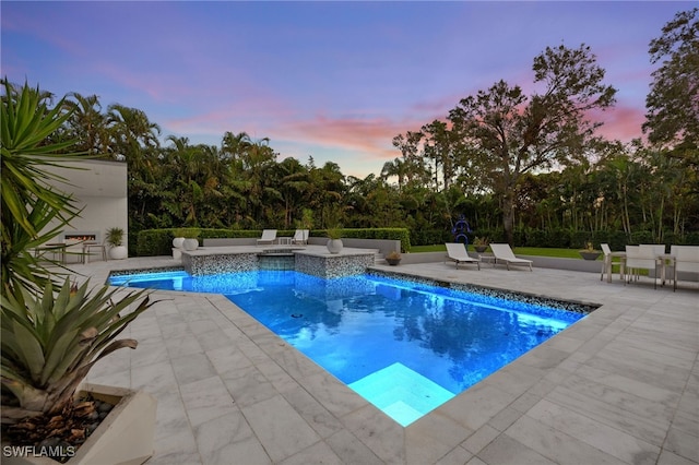 pool at dusk with a patio area and an in ground hot tub