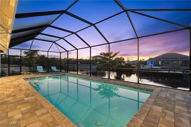 pool at dusk featuring a lanai, a patio area, and a water view