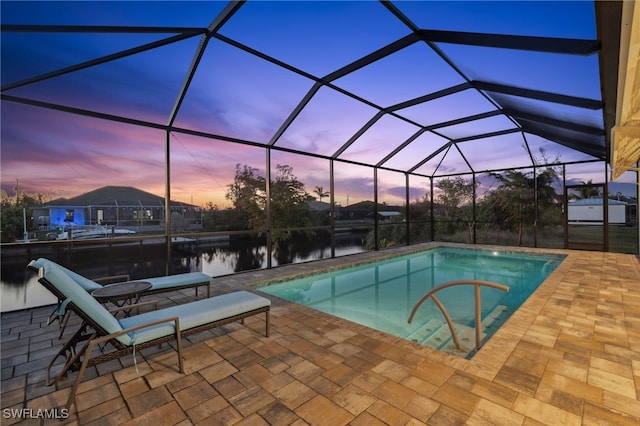 pool at dusk featuring a patio, a water view, and a lanai