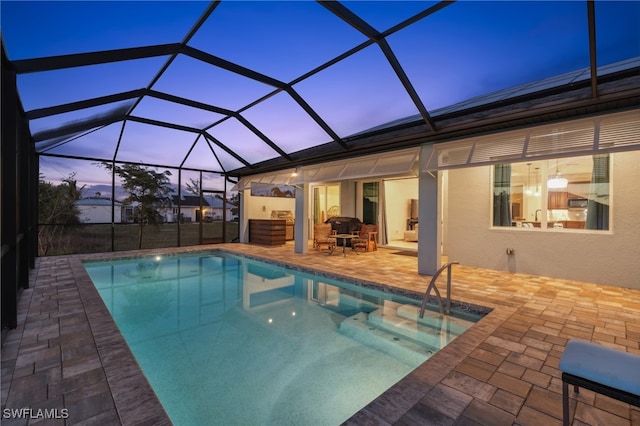 pool at dusk with glass enclosure and a patio area