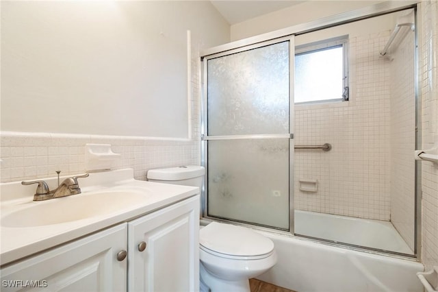 full bathroom featuring vanity, bath / shower combo with glass door, tile walls, and toilet