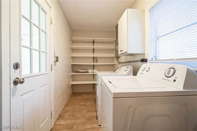 clothes washing area with a healthy amount of sunlight, washer and dryer, cabinets, and light wood-type flooring