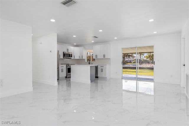 interior space with backsplash, sink, a center island, white cabinets, and appliances with stainless steel finishes