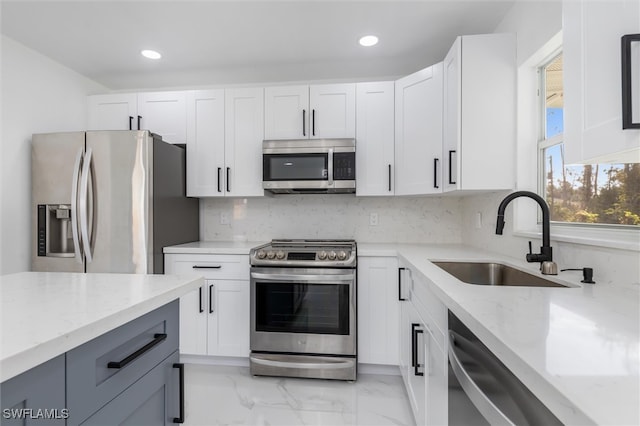 kitchen with stainless steel appliances, light stone countertops, sink, and white cabinets