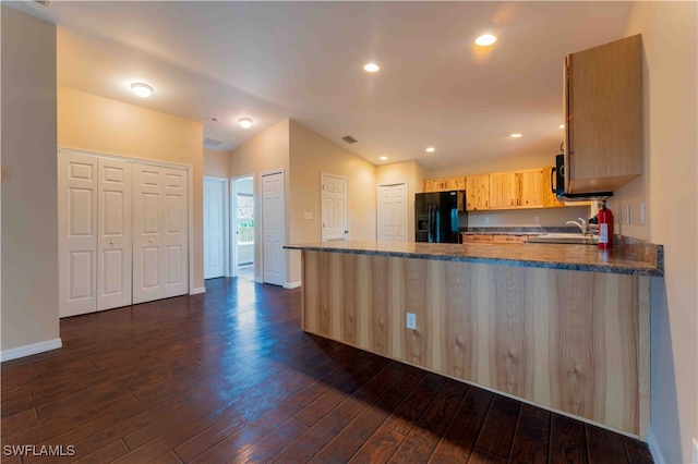 kitchen with light brown cabinets, dark wood-type flooring, kitchen peninsula, black appliances, and vaulted ceiling