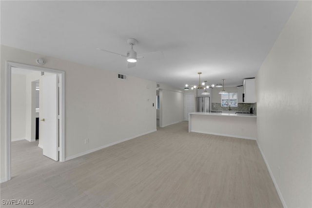 unfurnished living room with ceiling fan with notable chandelier and light wood-type flooring