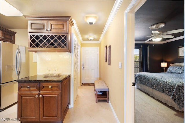 bar featuring stainless steel refrigerator with ice dispenser, ceiling fan, crown molding, and dark stone countertops