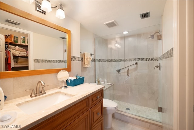 bathroom with a shower with door, decorative backsplash, vanity, toilet, and tile walls