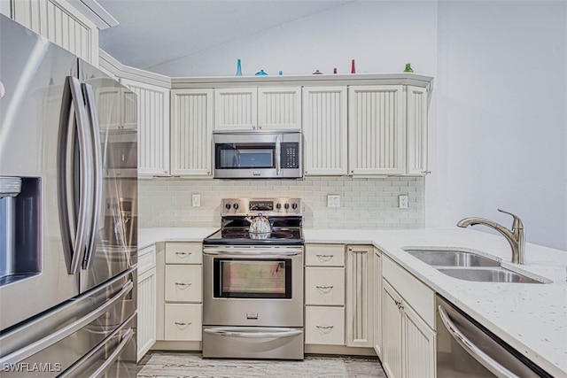 kitchen with lofted ceiling, decorative backsplash, sink, light stone countertops, and appliances with stainless steel finishes