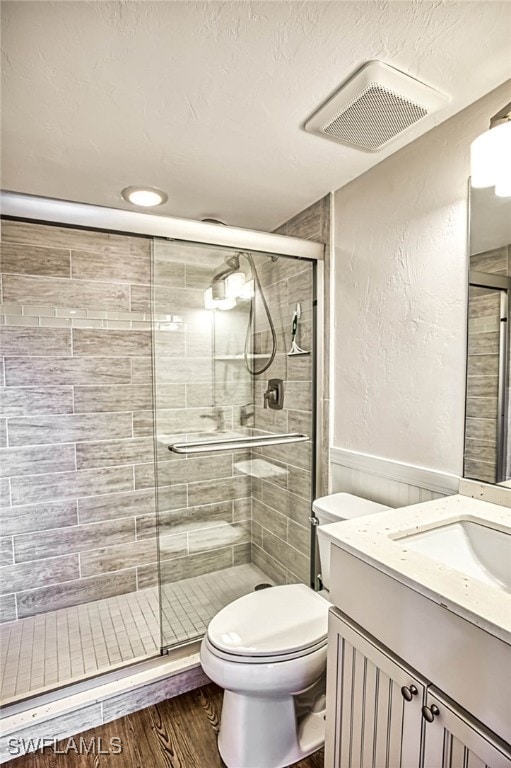 bathroom with a shower with door, vanity, wood-type flooring, and toilet