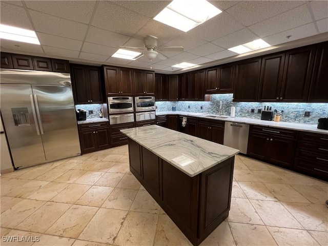 kitchen featuring a drop ceiling, ceiling fan, dark brown cabinets, a kitchen island, and stainless steel appliances