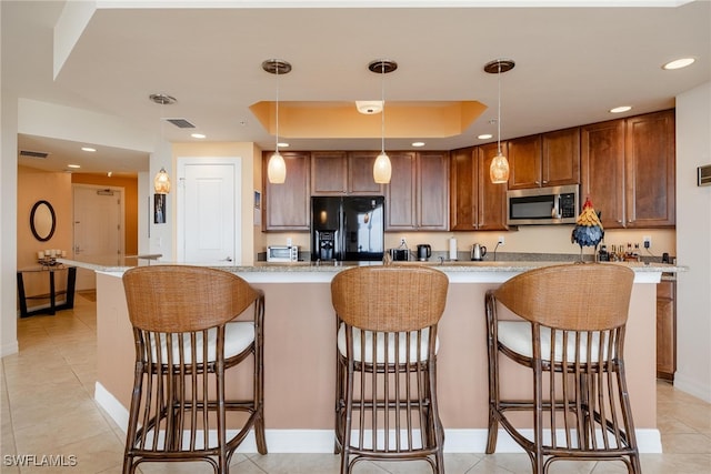 kitchen featuring a breakfast bar area, decorative light fixtures, black refrigerator with ice dispenser, a tray ceiling, and light stone countertops