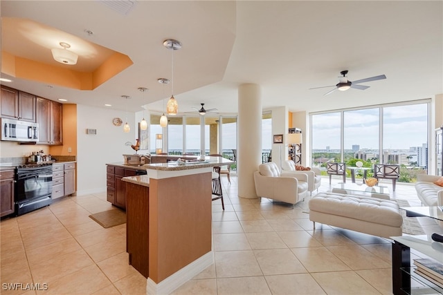 kitchen with hanging light fixtures, light tile patterned floors, a kitchen breakfast bar, a kitchen island with sink, and black range