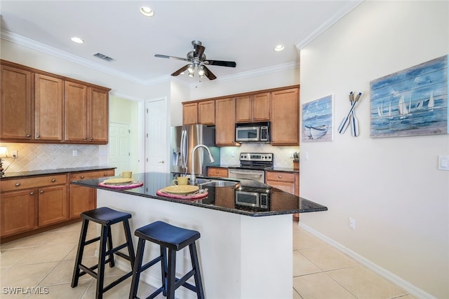 kitchen with appliances with stainless steel finishes, light tile patterned flooring, a center island with sink, and a kitchen breakfast bar