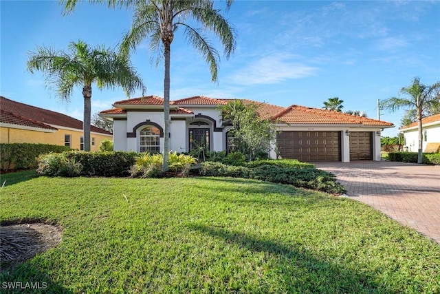 mediterranean / spanish home with decorative driveway, stucco siding, an attached garage, a tiled roof, and a front lawn