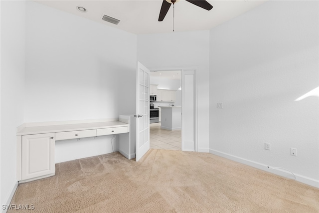 empty room featuring light colored carpet, built in desk, and ceiling fan