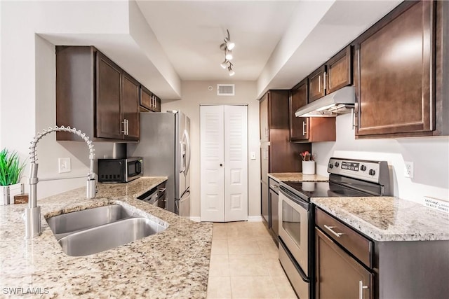 kitchen featuring appliances with stainless steel finishes, rail lighting, sink, light stone countertops, and dark brown cabinets