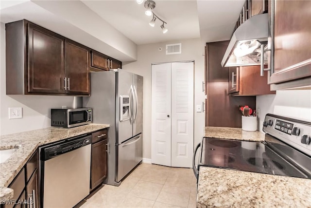 kitchen with dark brown cabinetry, track lighting, light stone countertops, and appliances with stainless steel finishes