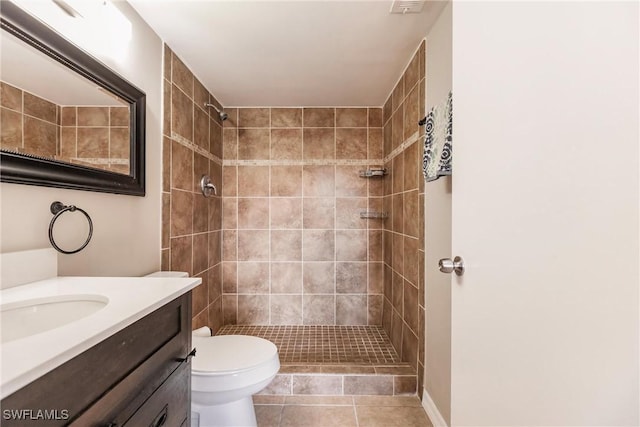 bathroom with tile patterned flooring, vanity, a tile shower, and toilet