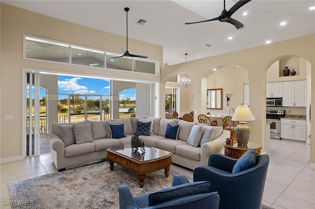 living room featuring ceiling fan with notable chandelier, light tile patterned flooring, and a towering ceiling