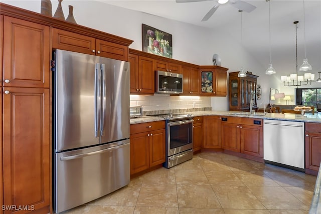 kitchen with sink, stainless steel appliances, decorative light fixtures, light stone counters, and high vaulted ceiling