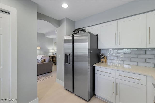 kitchen with stainless steel fridge, white cabinetry, and backsplash